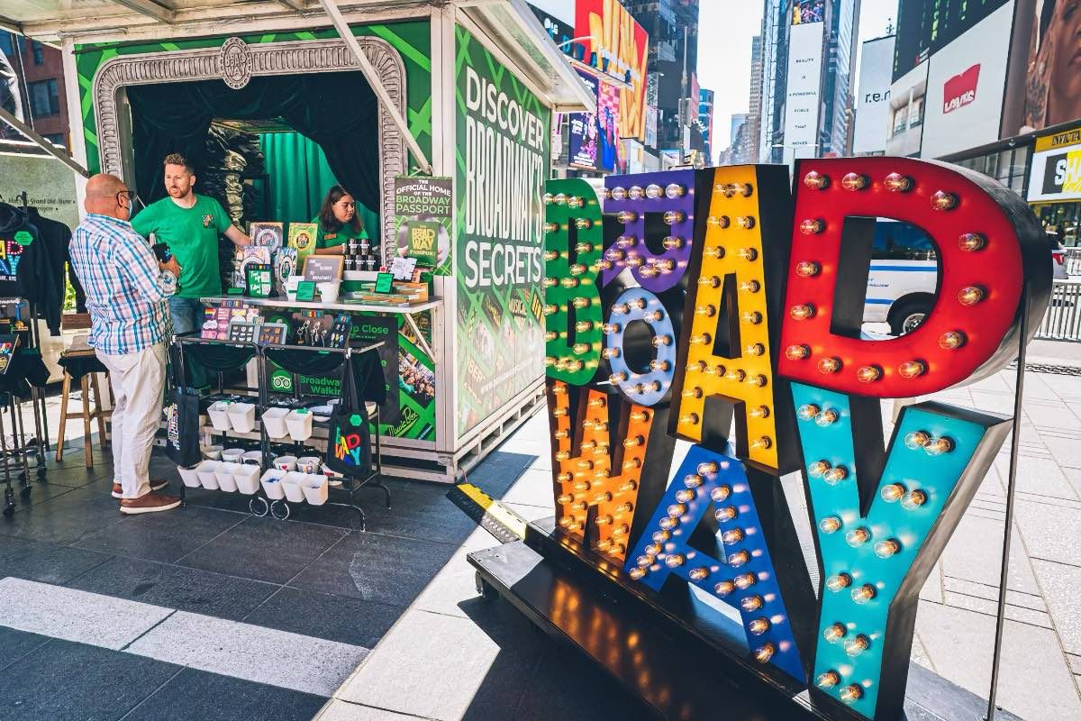 The Broadway Gift Shop's kiosk in Times Square, beside the illuminated BROADWAY marquee sign
