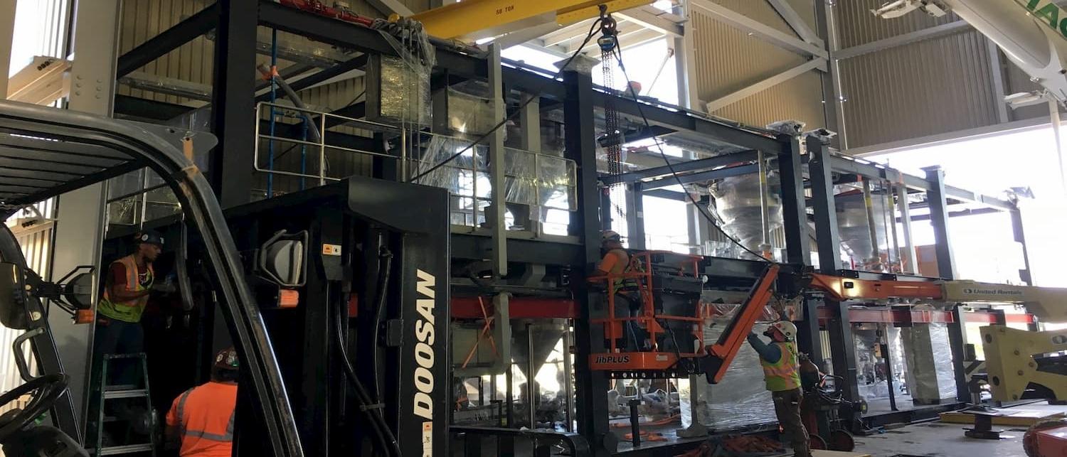 Sack Company crew moving large industrial equipment with a forklift and crane.