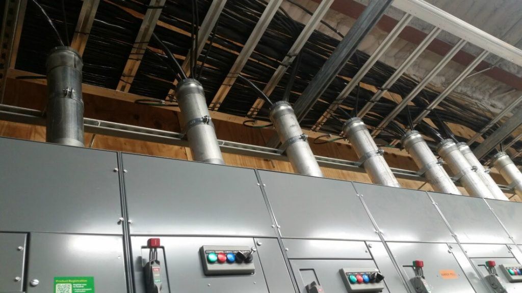 Row of electrical switchgear panels with overhead conduit in an industrial electrical room.