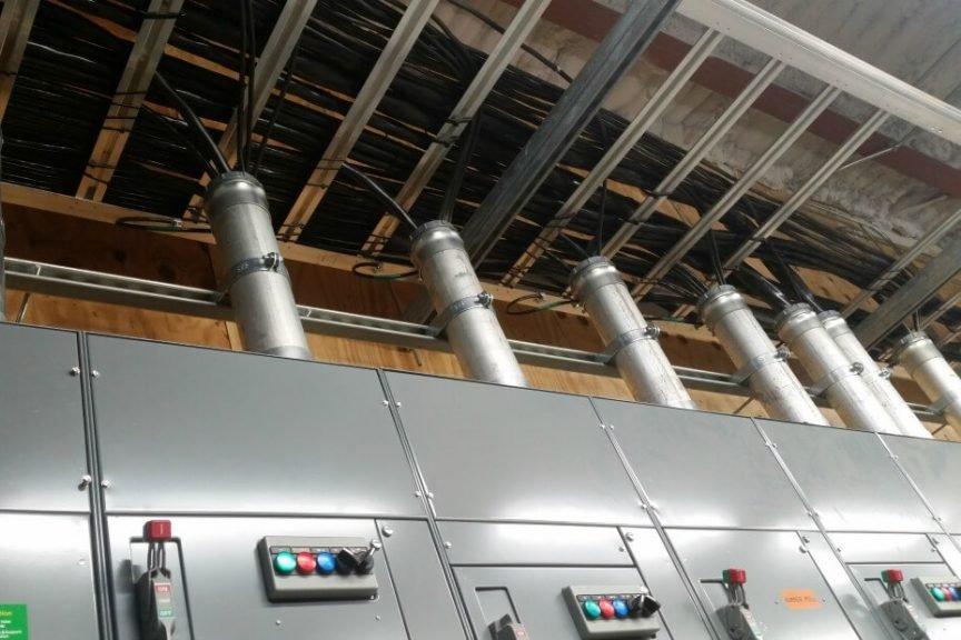 Row of electrical switchgear panels with overhead conduit in an industrial electrical room.
