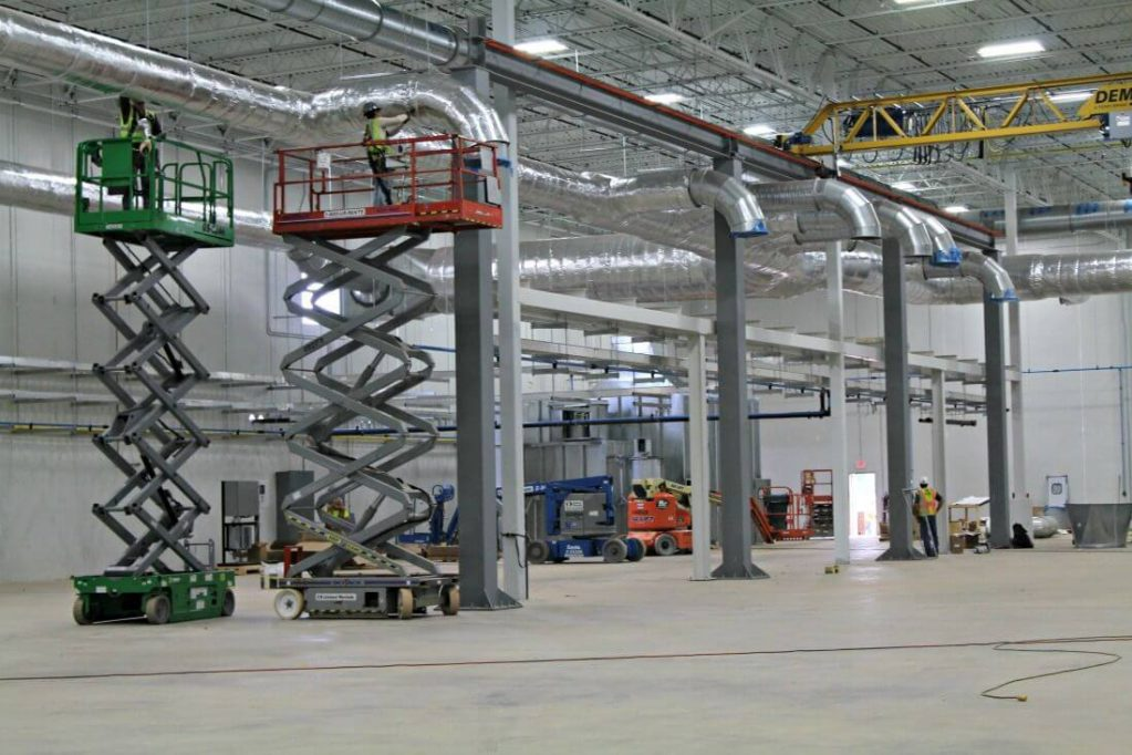 Sack Company crews on scissor lifts installing ductwork and piping inside a new manufacturing plant
