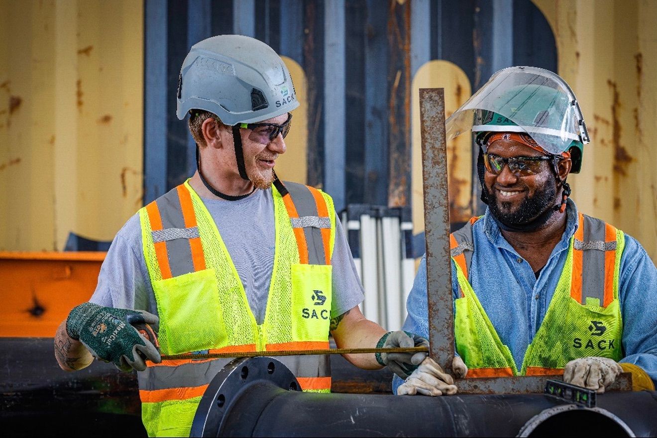 Two Sack Company workers in hard hats and safety vests fitting pipe.