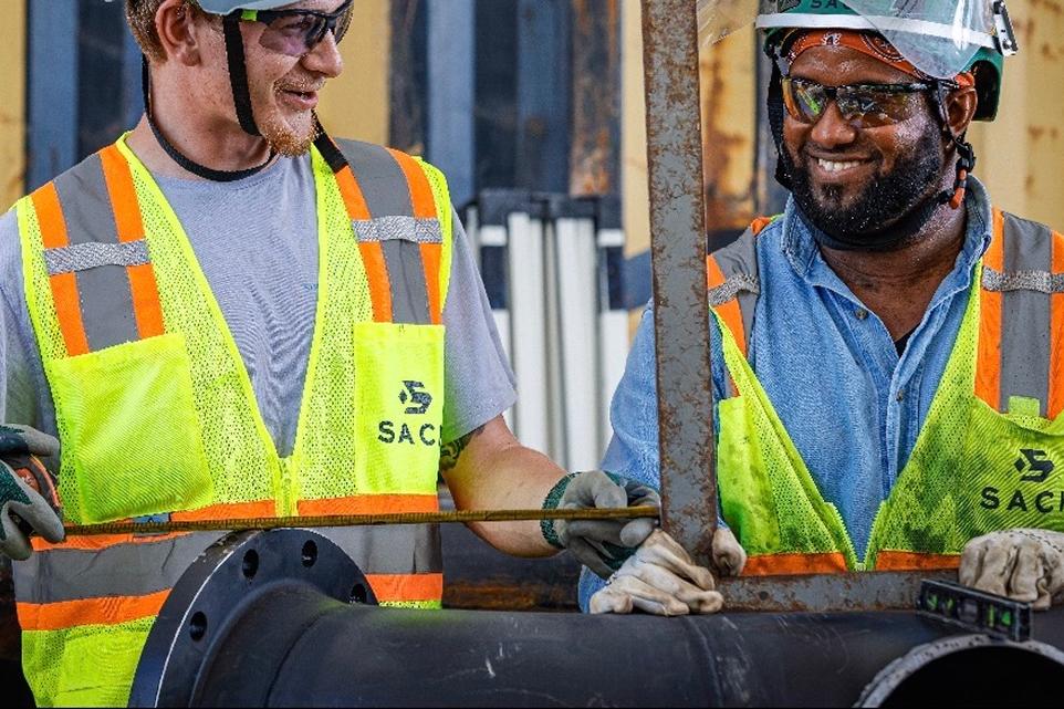 Two Sack Company workers in hard hats and safety vests fitting pipe.