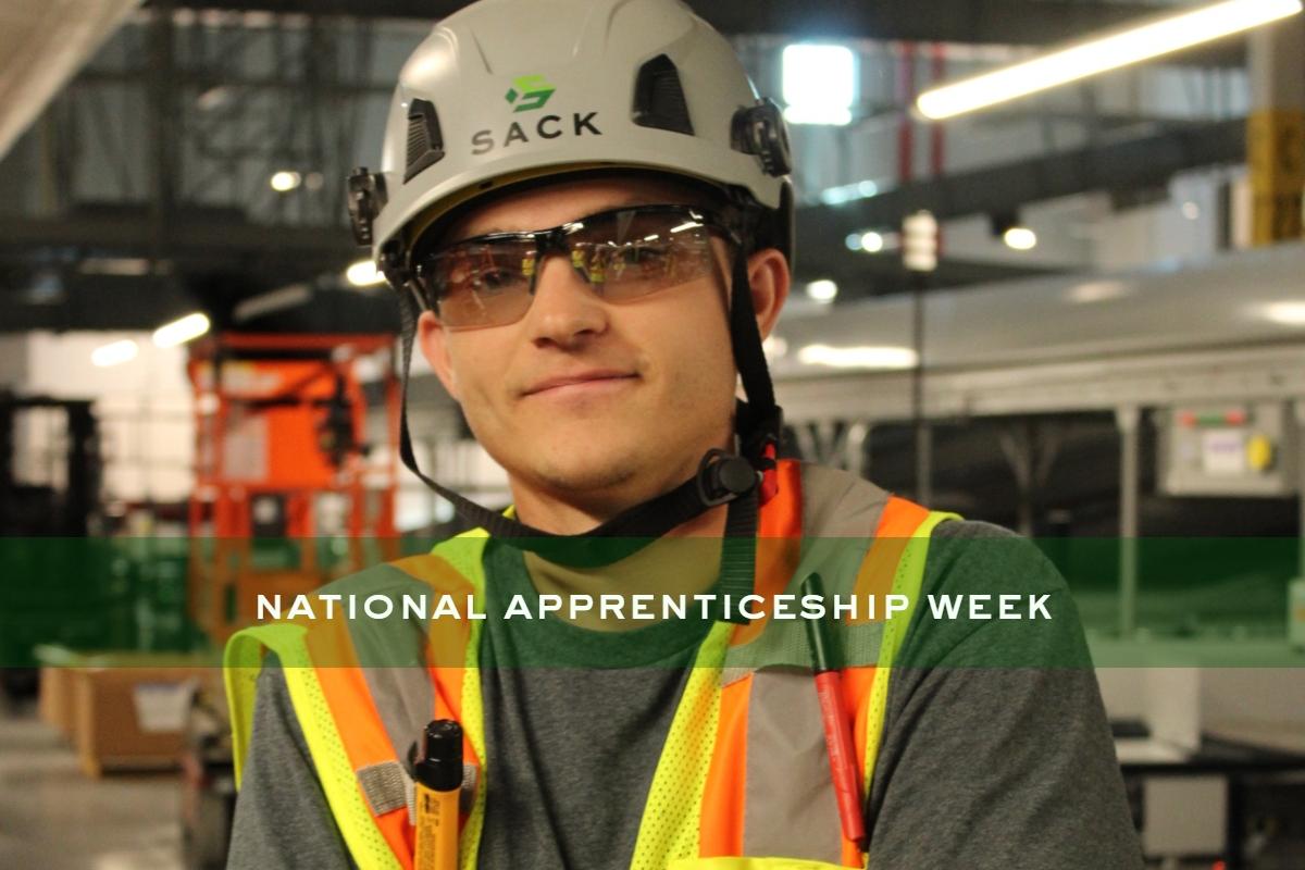 Apprentice wearing safety gear and Sack Company hard hat during National Apprenticeship Week at industrial jobsite.