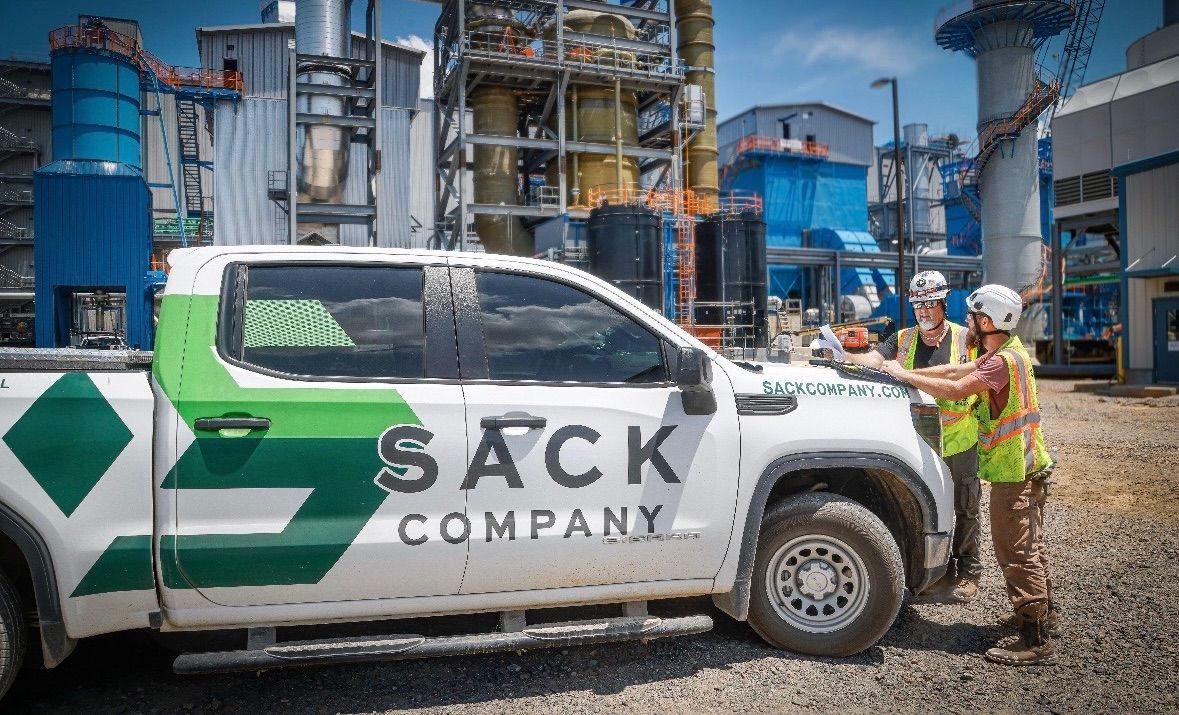 Sack Company truck with two workers in hard hats at an industrial plant.