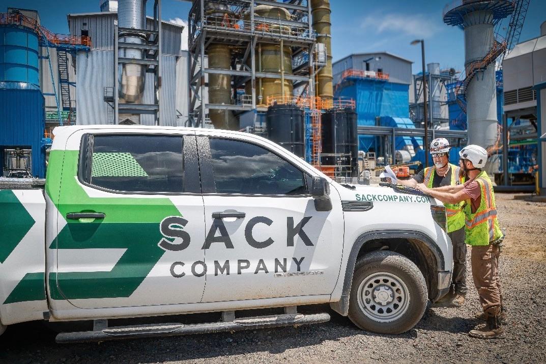 Sack Company truck with two workers in hard hats at an industrial plant.