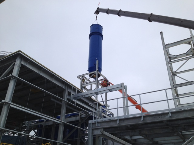 Crane lowering a large blue process vessel into the steel frame of a pigment plant