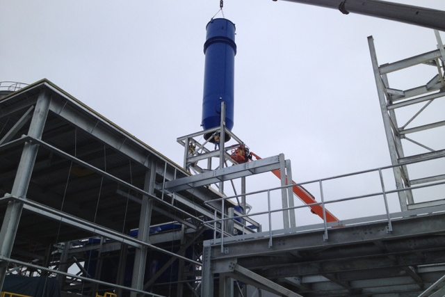 Crane lowering a large blue process vessel into the steel frame of a pigment plant