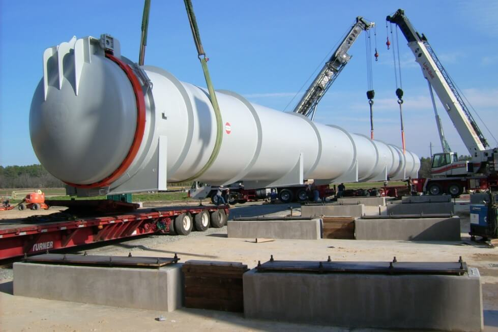 Two cranes setting a large autoclave onto concrete foundations at an industrial site