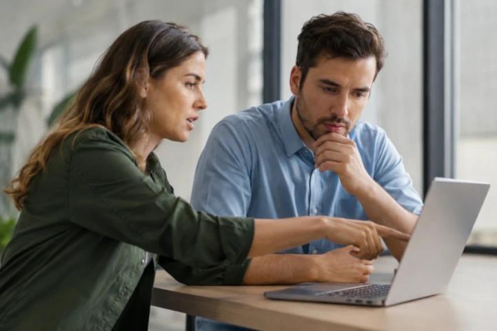 Zwei Kolleg:innen besprechen konzentriert Inhalte am Laptop in modernem Büro bei natürlichem Licht.