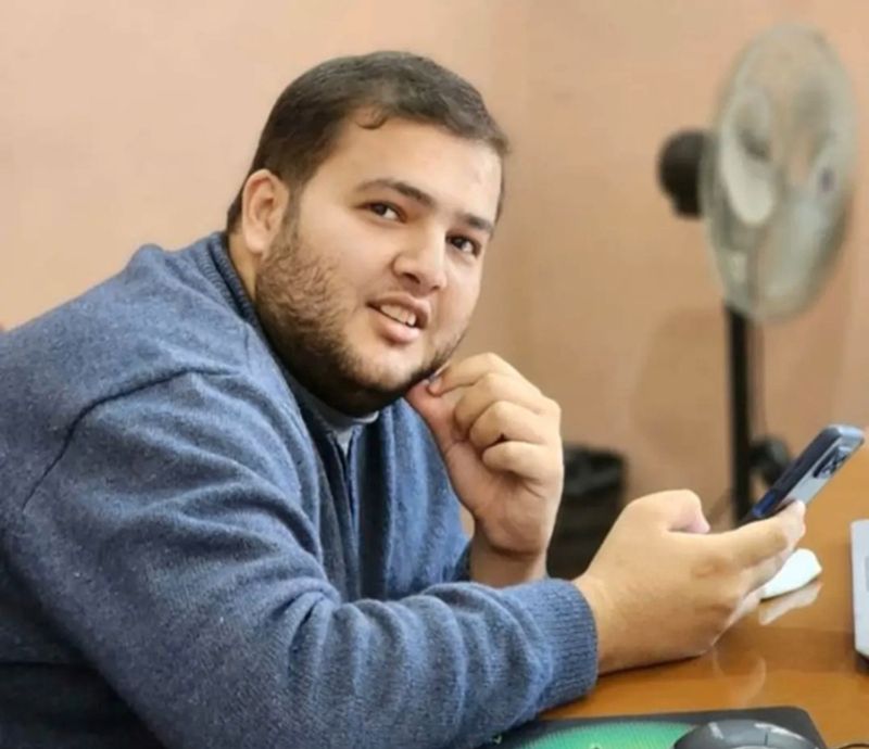 Mahmoud holding a phone while looking at the camera