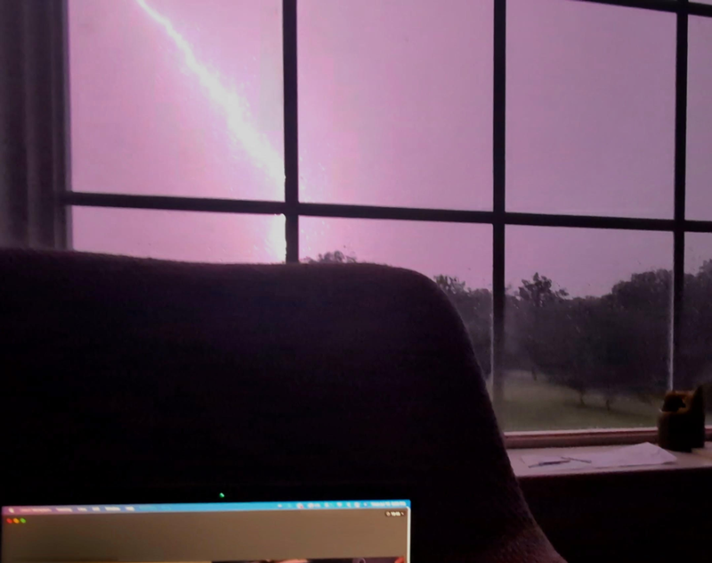 A bolt of lightning as seen through a window, against a purple sky.