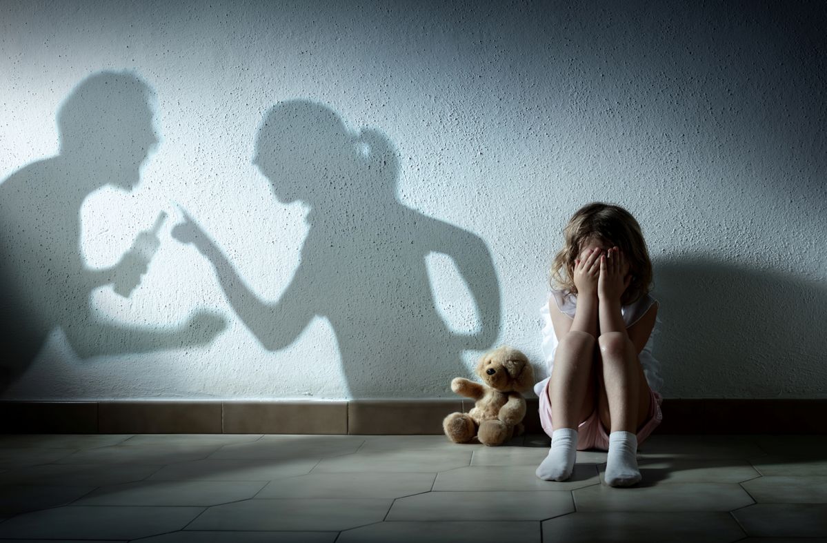 Una niña triste, con las sombras de sus padres peleando.