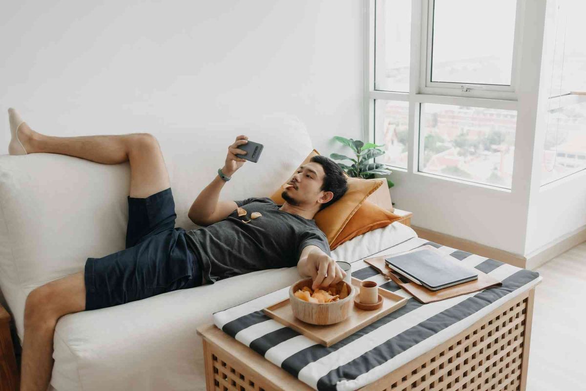 Hombre acostada en un sillón, viendo memes, y redes sociales