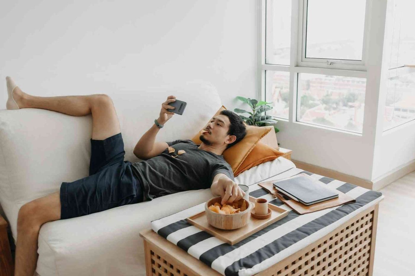 Hombre acostada en un sillón, viendo memes, y redes sociales