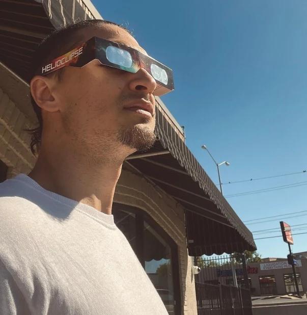 man wearing helioclipse glasses looking at solar eclipse urban street — people viewing the eclipse with protective glasses