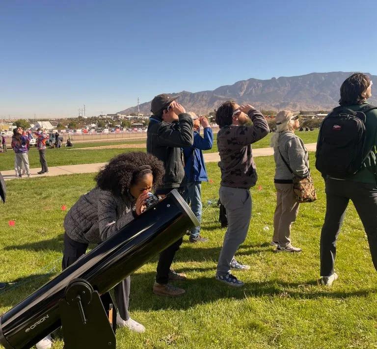People observe an annular eclipse with eclipse glasses and a solar-safe telescope setup.