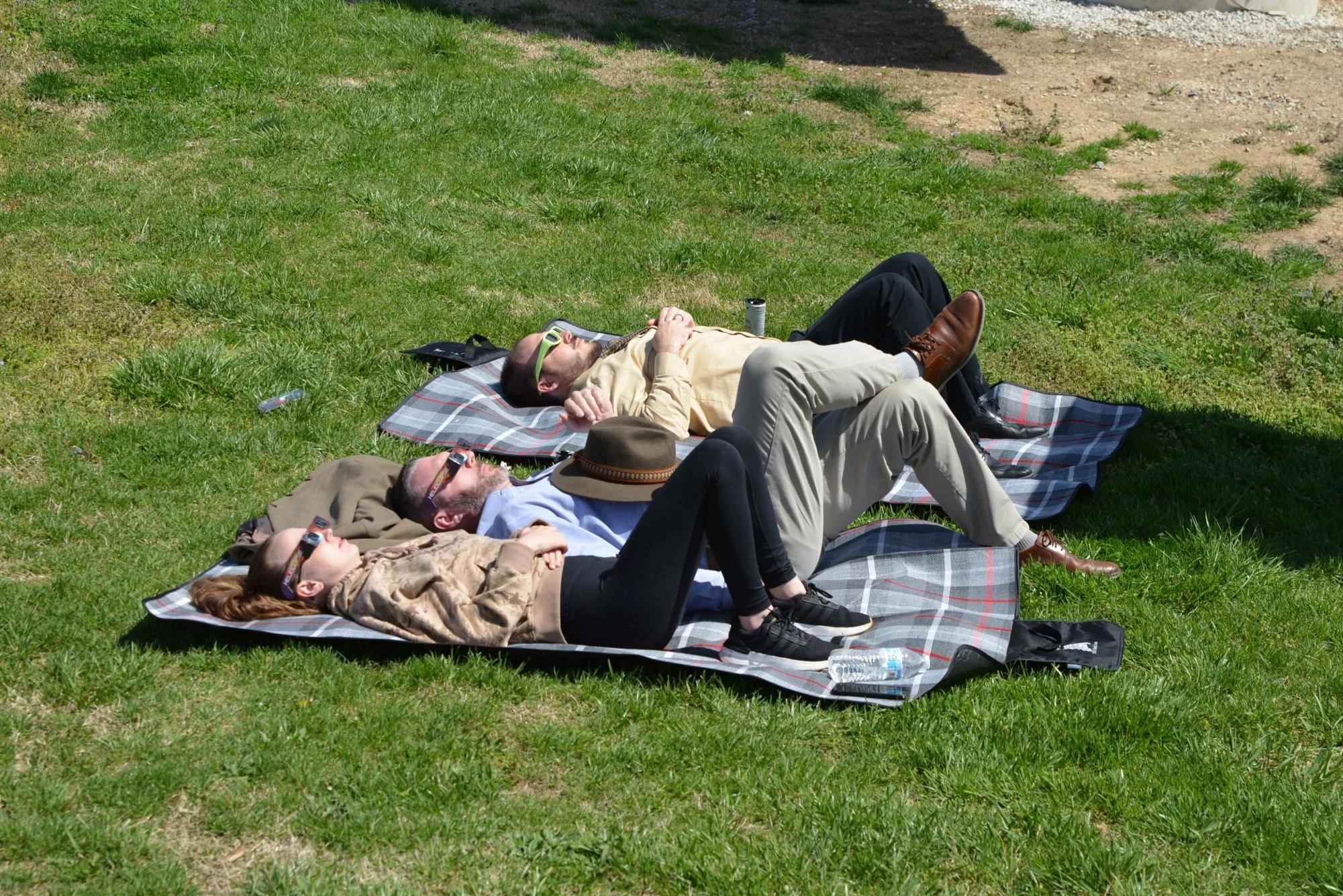 group of friends relaxing on blanket viewing solar eclipse glasses park — people viewing the eclipse with protective glasses
