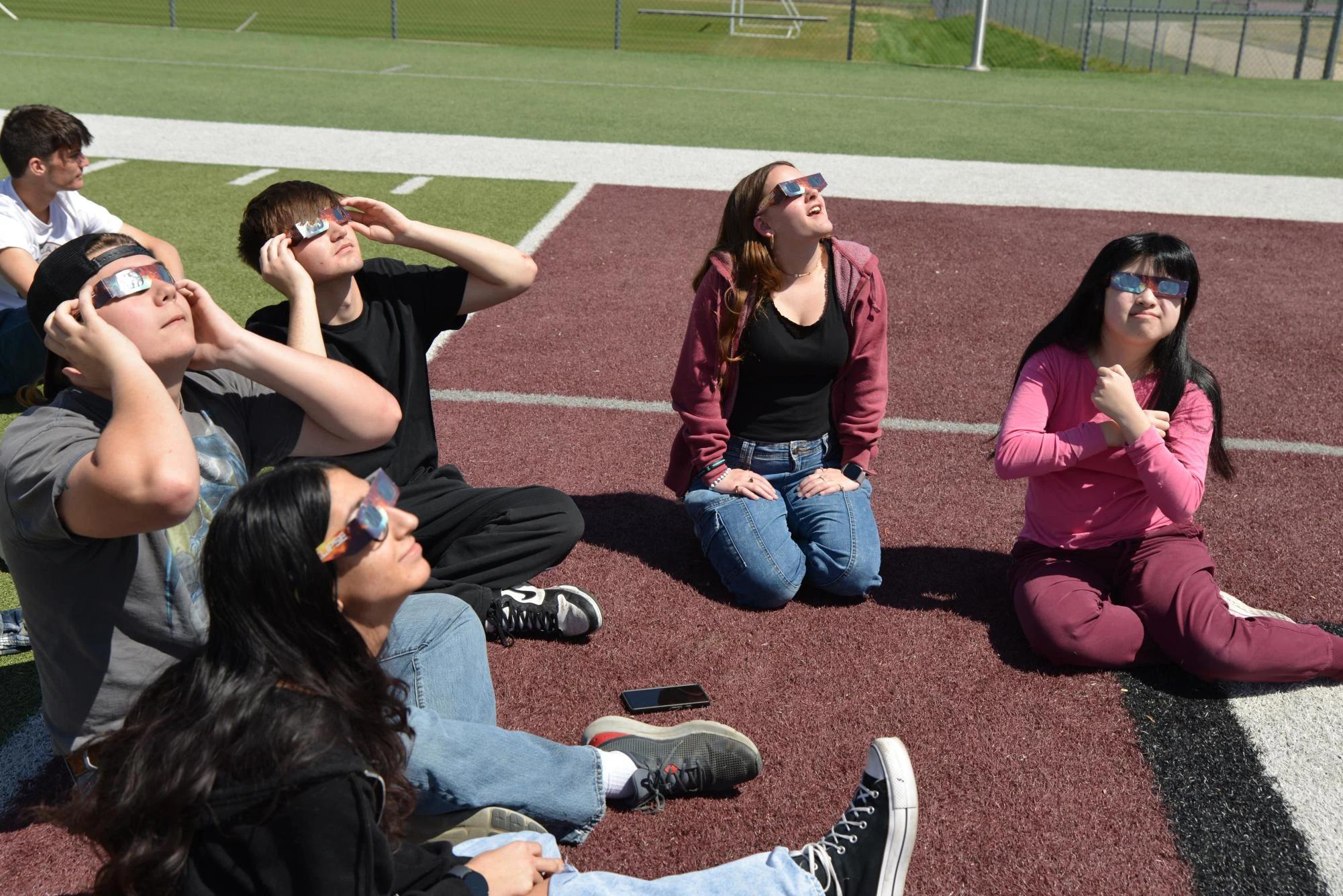 diverse group students sitting field watching solar eclipse glasses — people viewing the eclipse with protective glasses