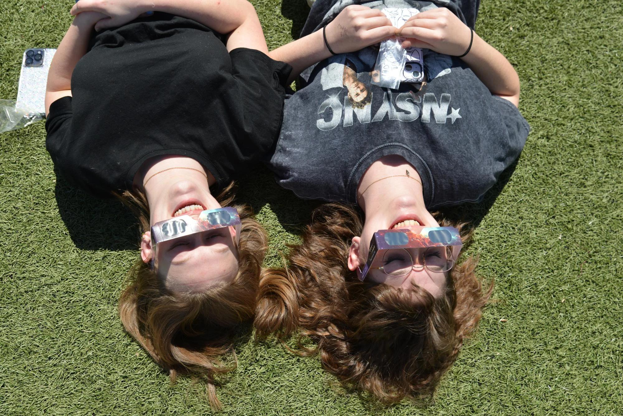 top view two girls lying on grass wearing solar eclipse glasses — people viewing the eclipse with protective glasses