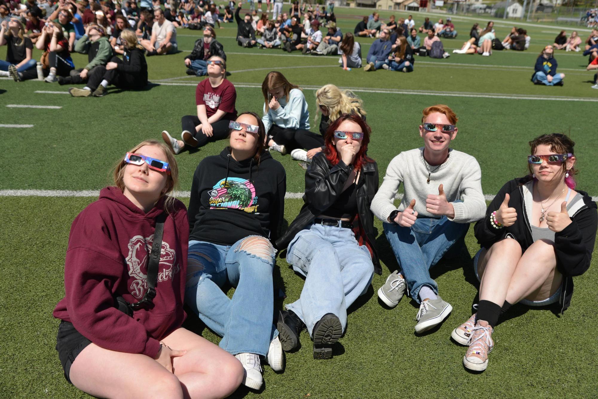 friends watching solar eclipse sitting together outdoor school event — people viewing the eclipse with protective glasses
