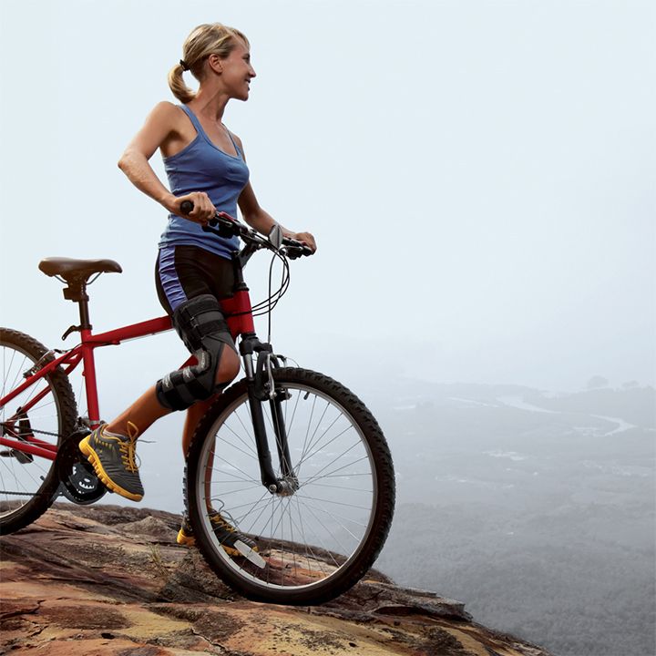 Die DonJoy Playmaker 2 Spacer Wrap Kniebandage wird von einer Frau beim Mountainbiken getragen.