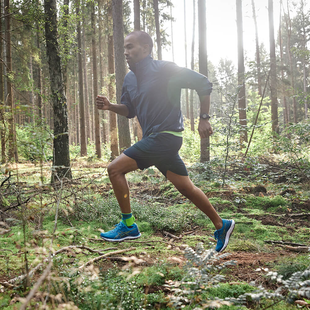 Mann läuft im Wald mit der Bauerfeind Sports Sprunggelenkbandage in Riviera Blau