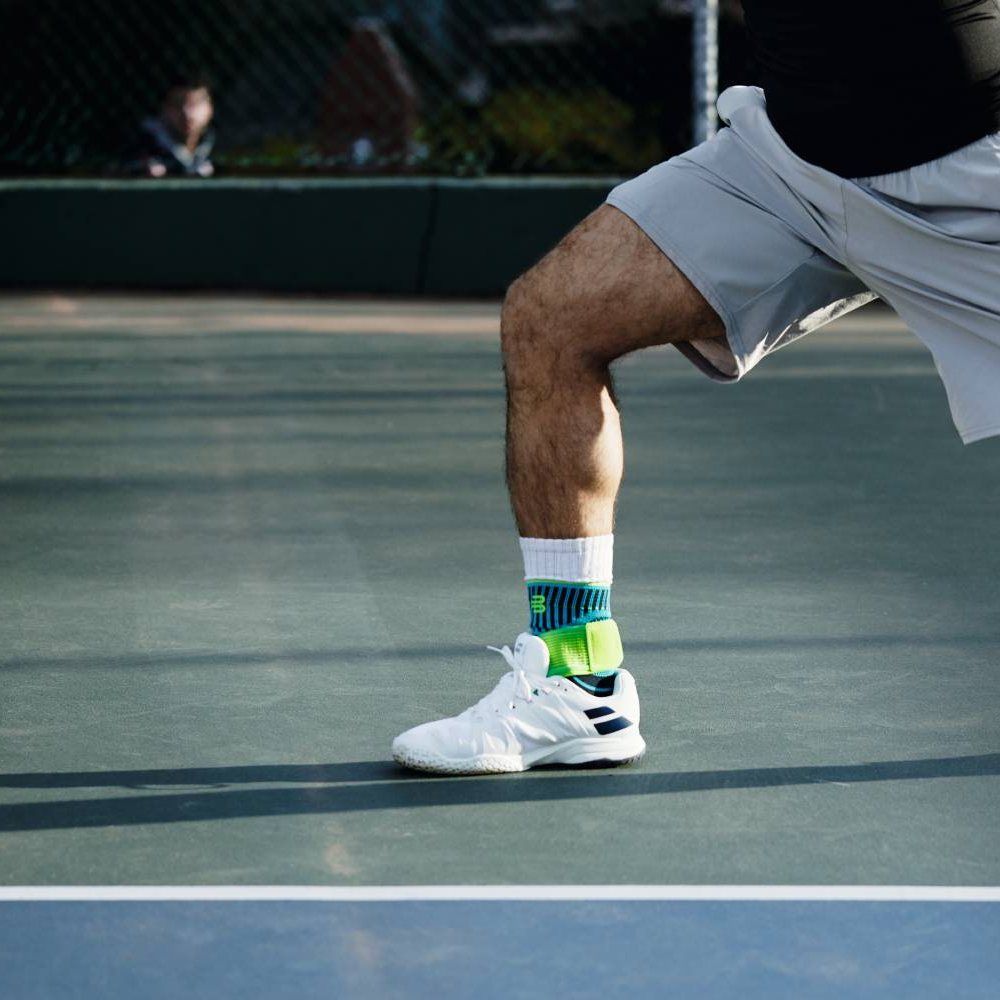 Ein Mann spielt Tennis und trägt die Bauerfeind Sports Sprunggelenkbandage in Riviera Blau