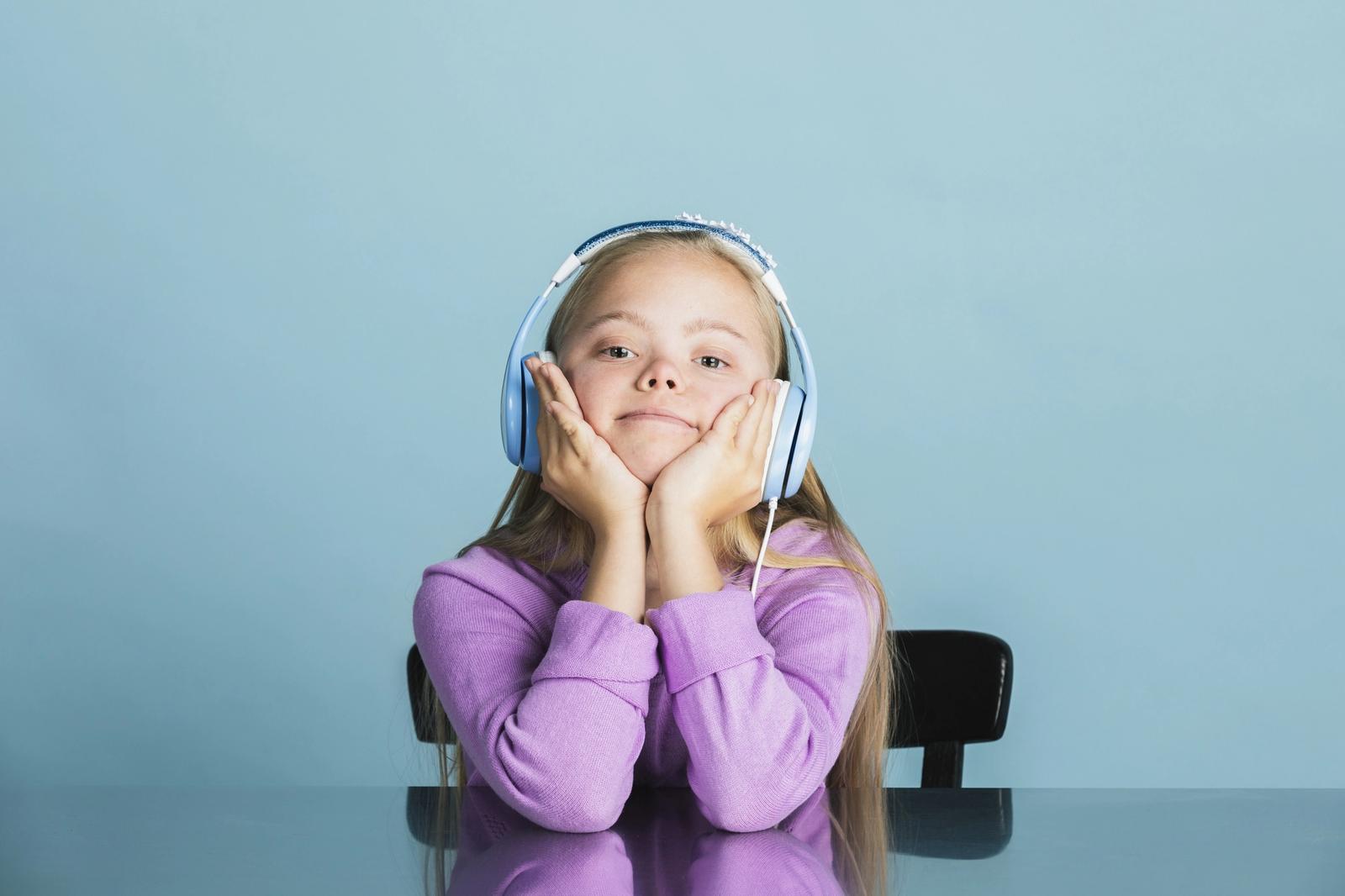 A young girl with Down syndrome wearing headphones and sitting at a table