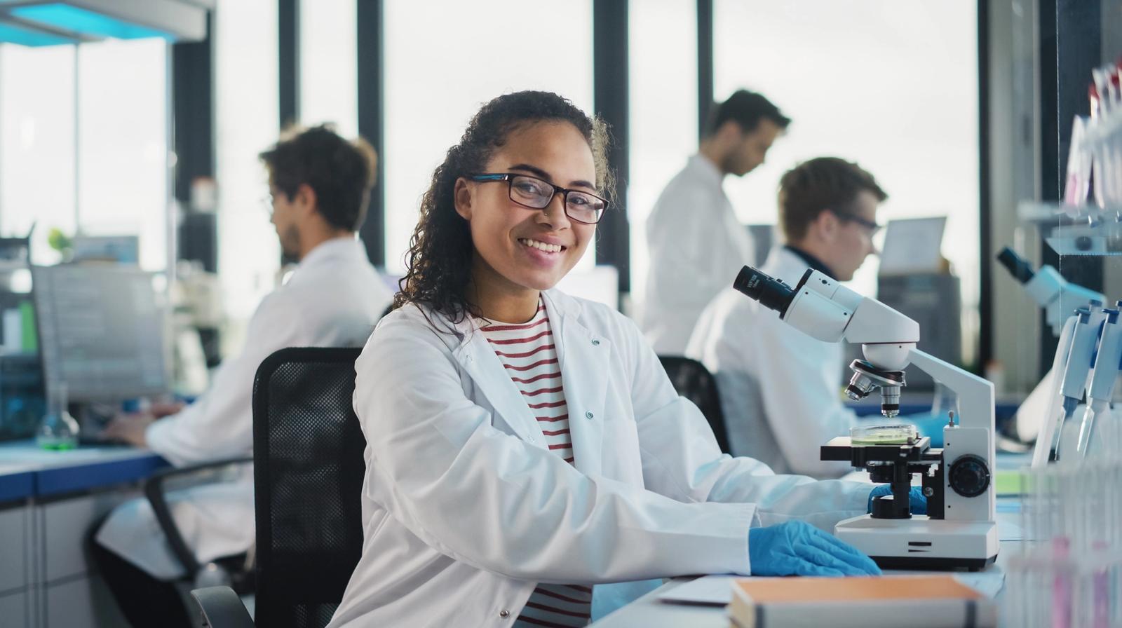A scientist on white lab coat sitting in front of microscope