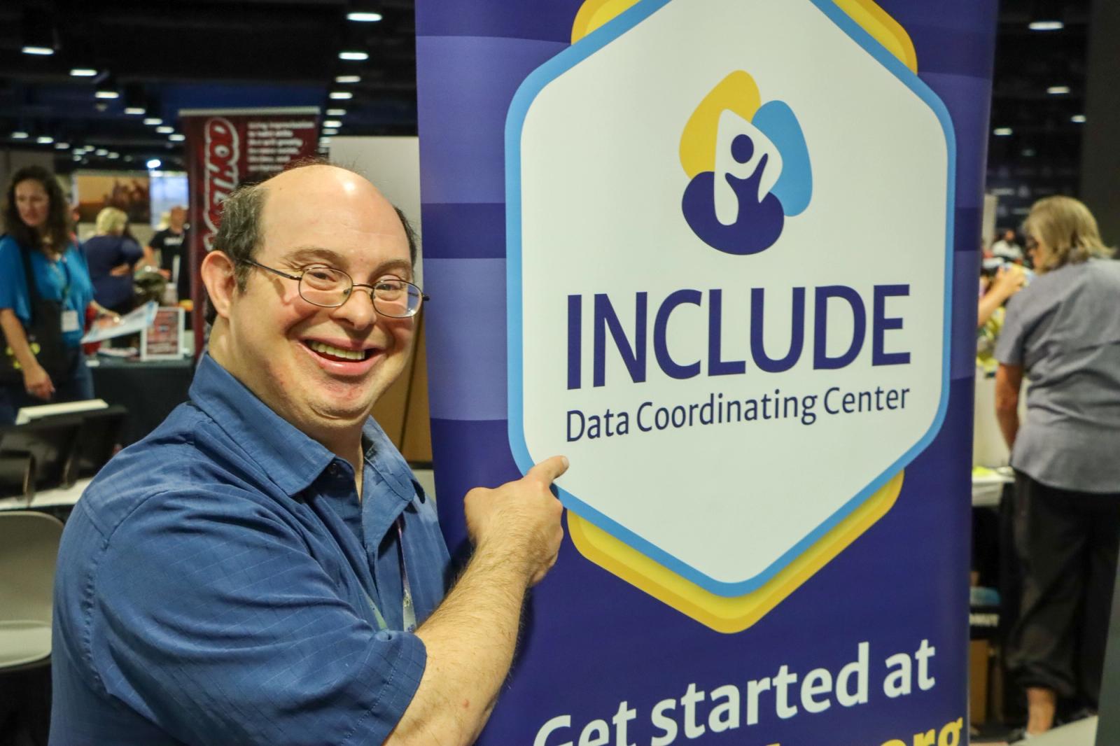 Self-advocate standing beside and pointing to the INCLUDE DCC banner