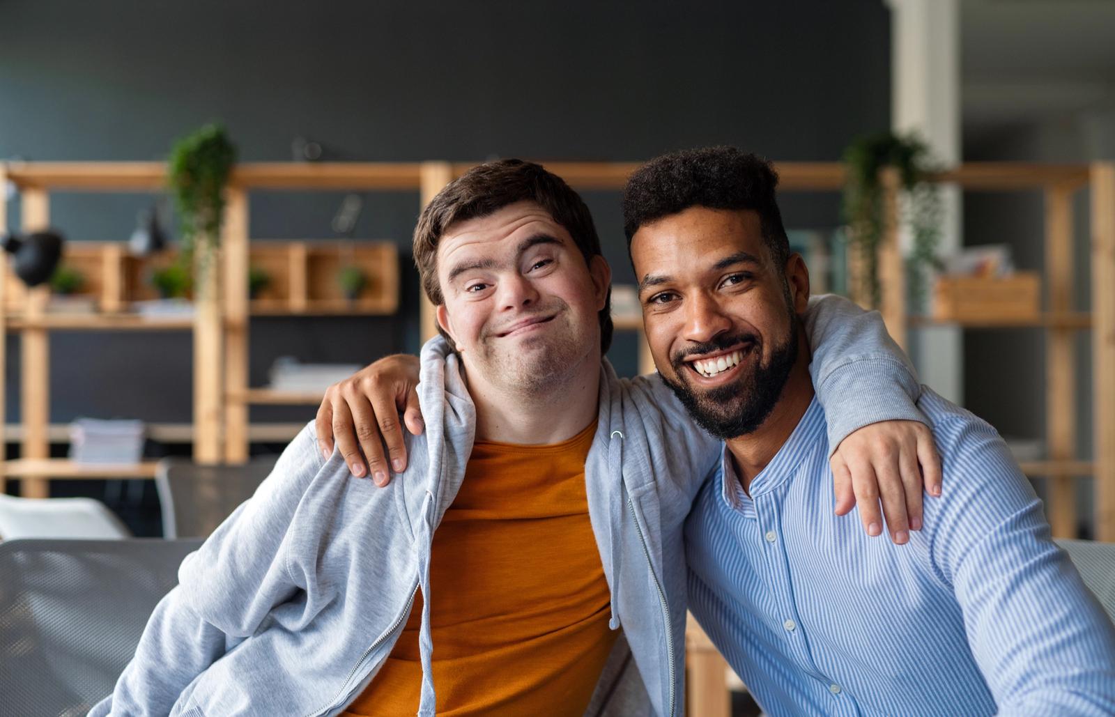 A young man with Down syndrome and a man without Down syndrome with their arms around each others' shoulders
