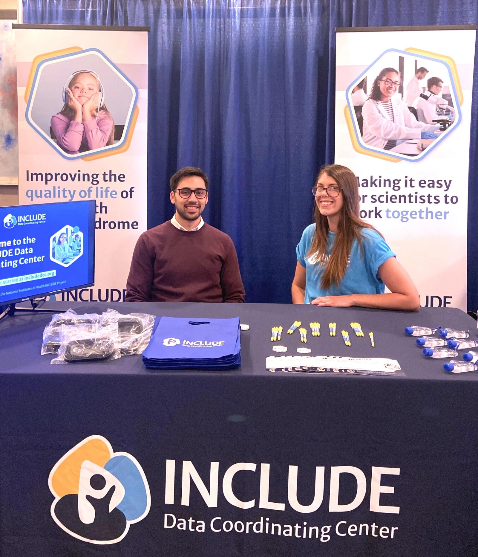 Two INCLUDE DCC team members sitting at the INCLUDE DCC booth at the T21RS Conference
