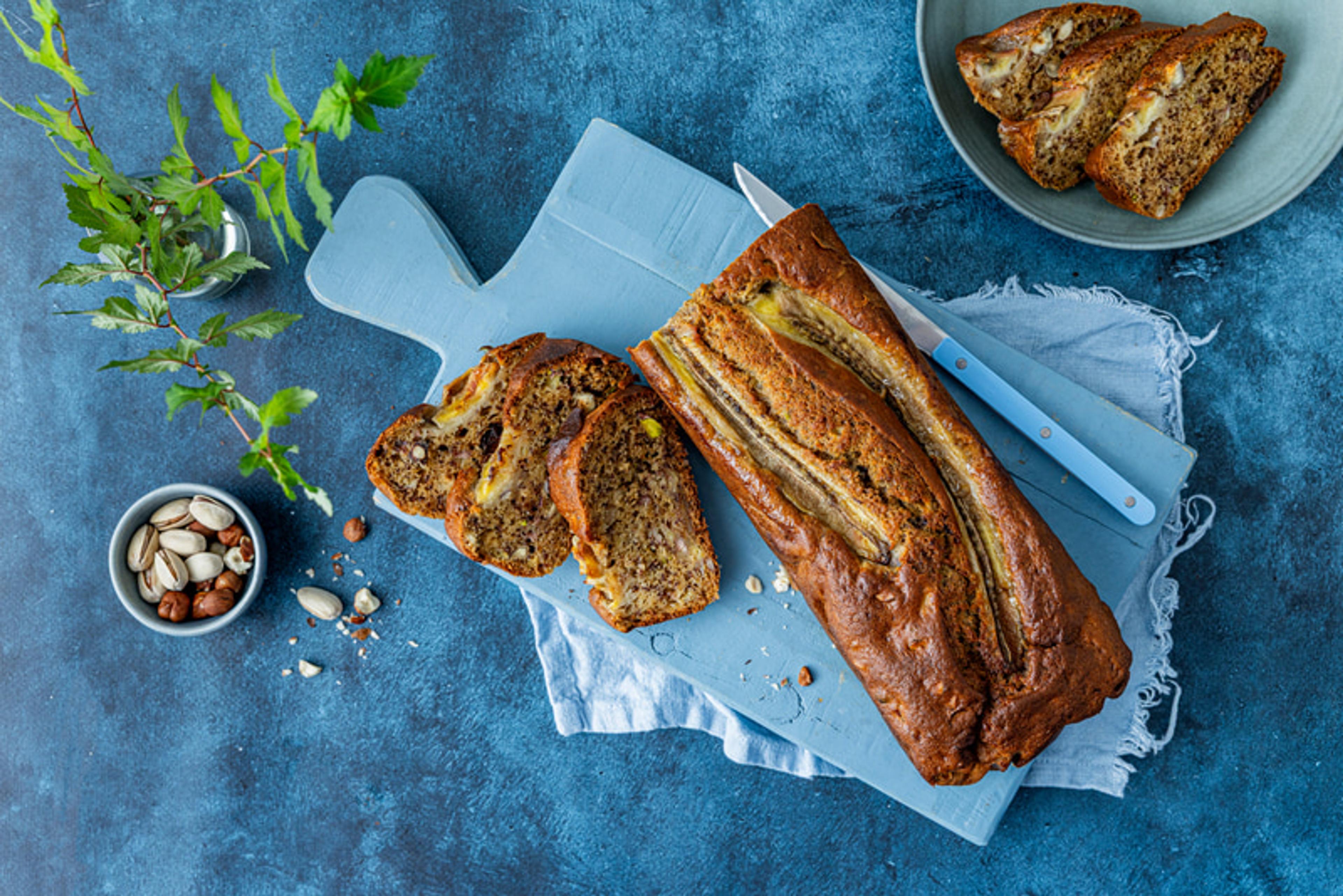 Bananbrød på et vord med blå bakgrunn og pistasjnøtter i en skål
