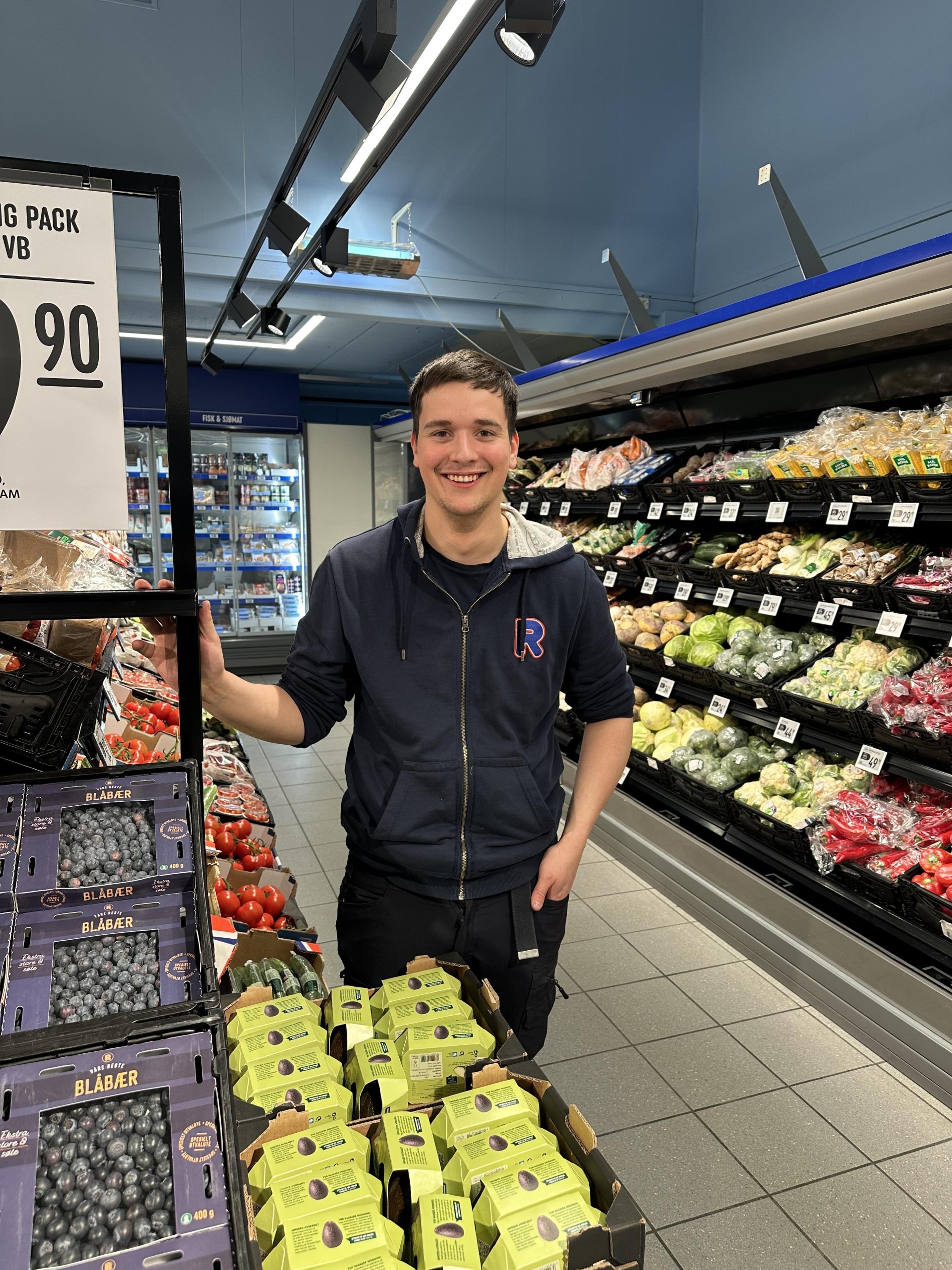 REMA-ansatt smiler foran frukt og grønt-avdeling