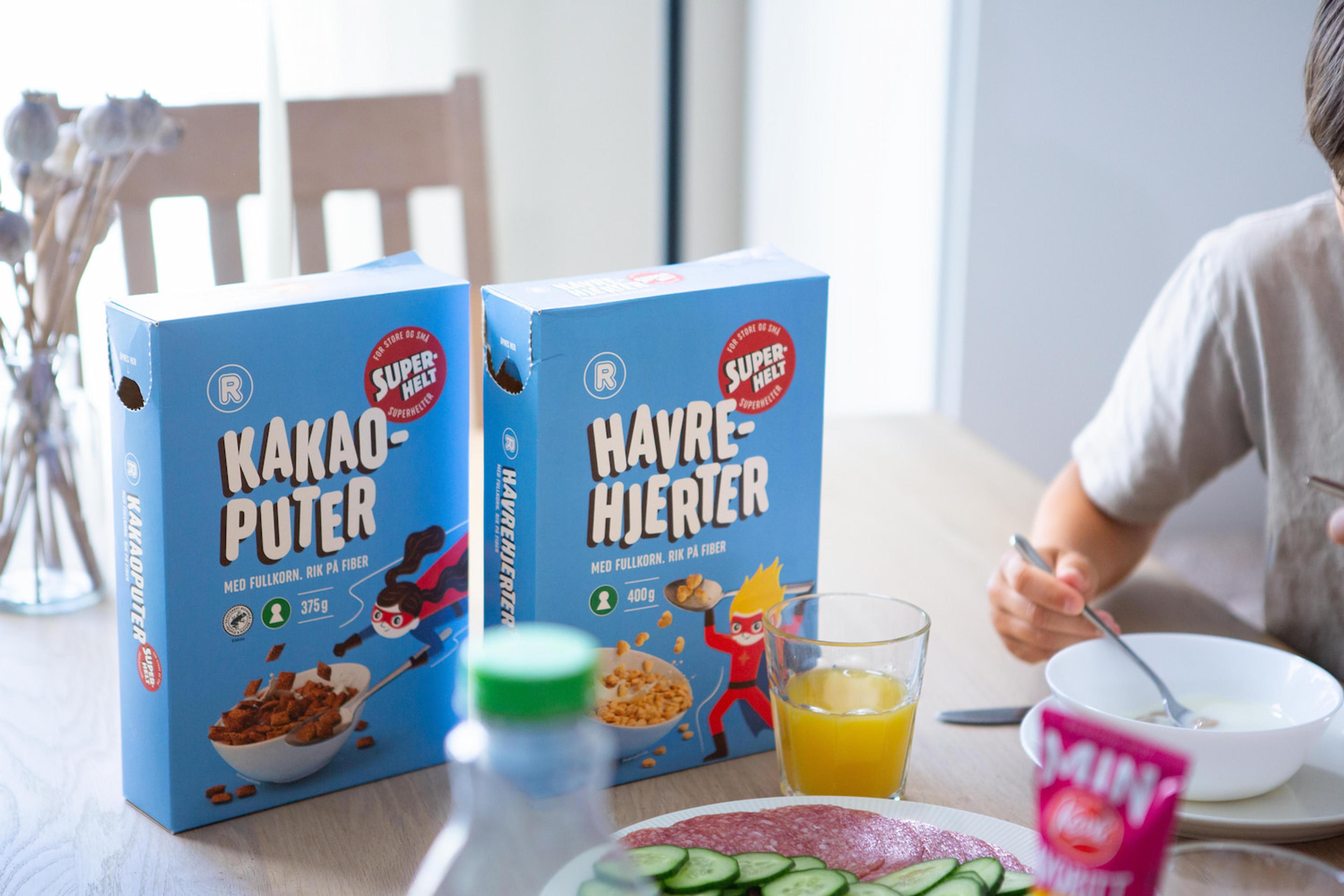Superheltproduktene Kakaoputer og Havrehjerter på et frokostbord med et barn som sitter og spiser på siden.