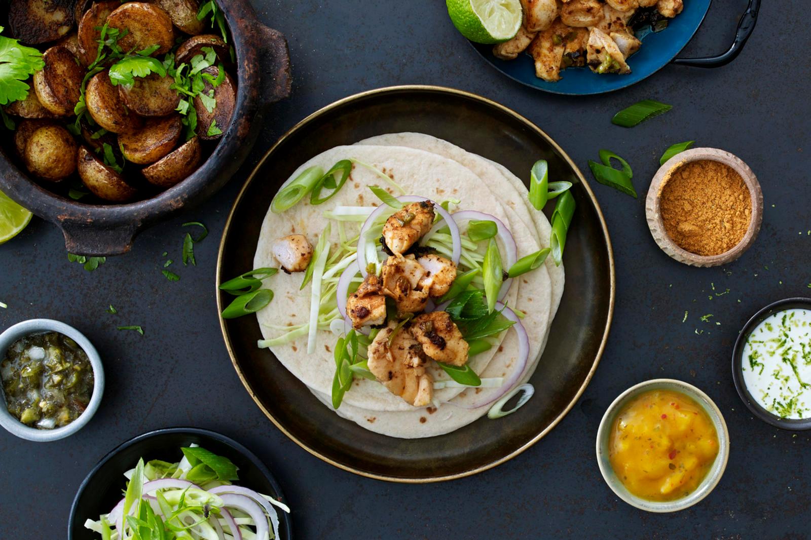 Fisketaco: tacolefse med vårløk, rødløk, koriander, torsk i biter. Rundt er det små skåler med mangosalsa, rømme og Salsa Piccante.
