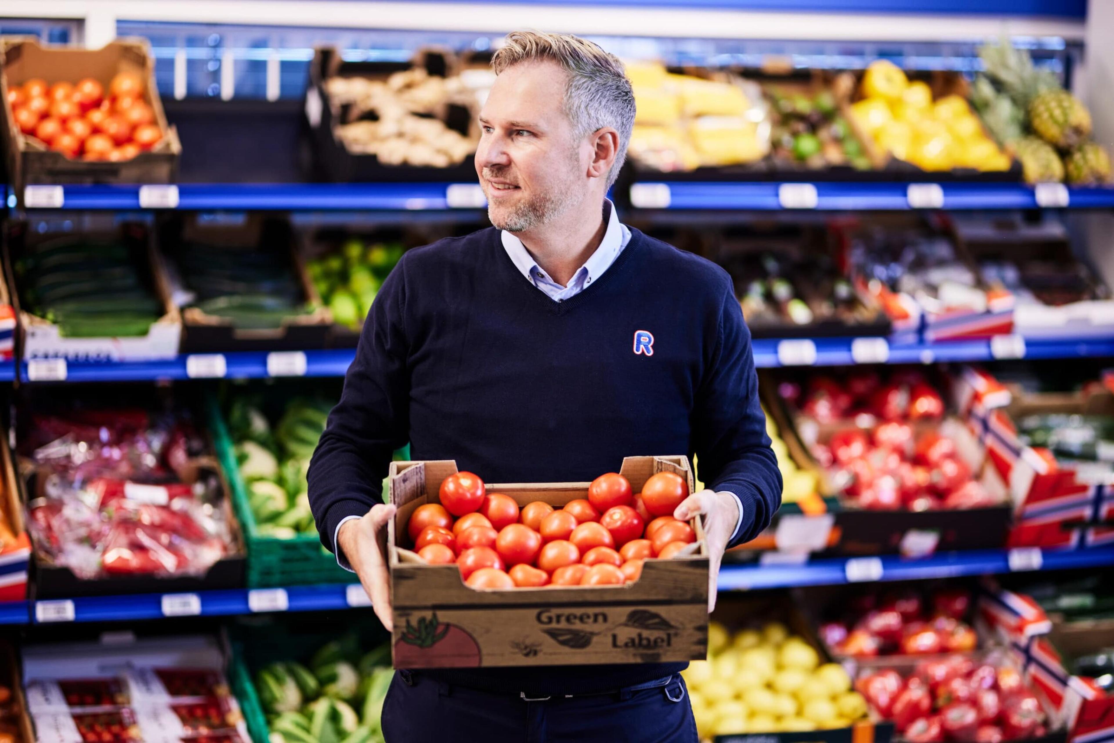 Mann som står med en kasse tomater i hånden