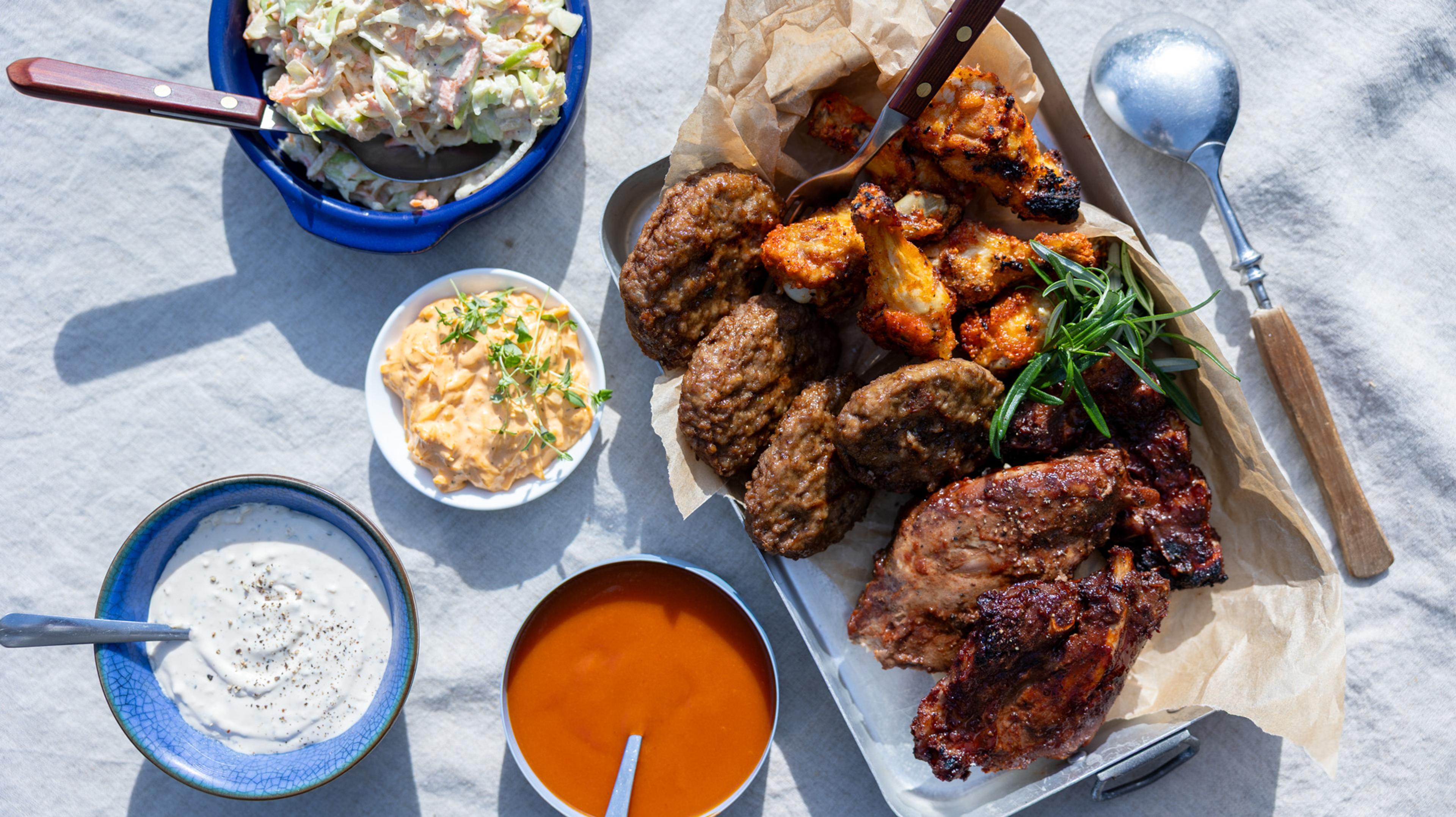mixed grill fra usa med sliders, kyllingvinger og spareribs ligger på et fat med flere dipper stilt opp rundt