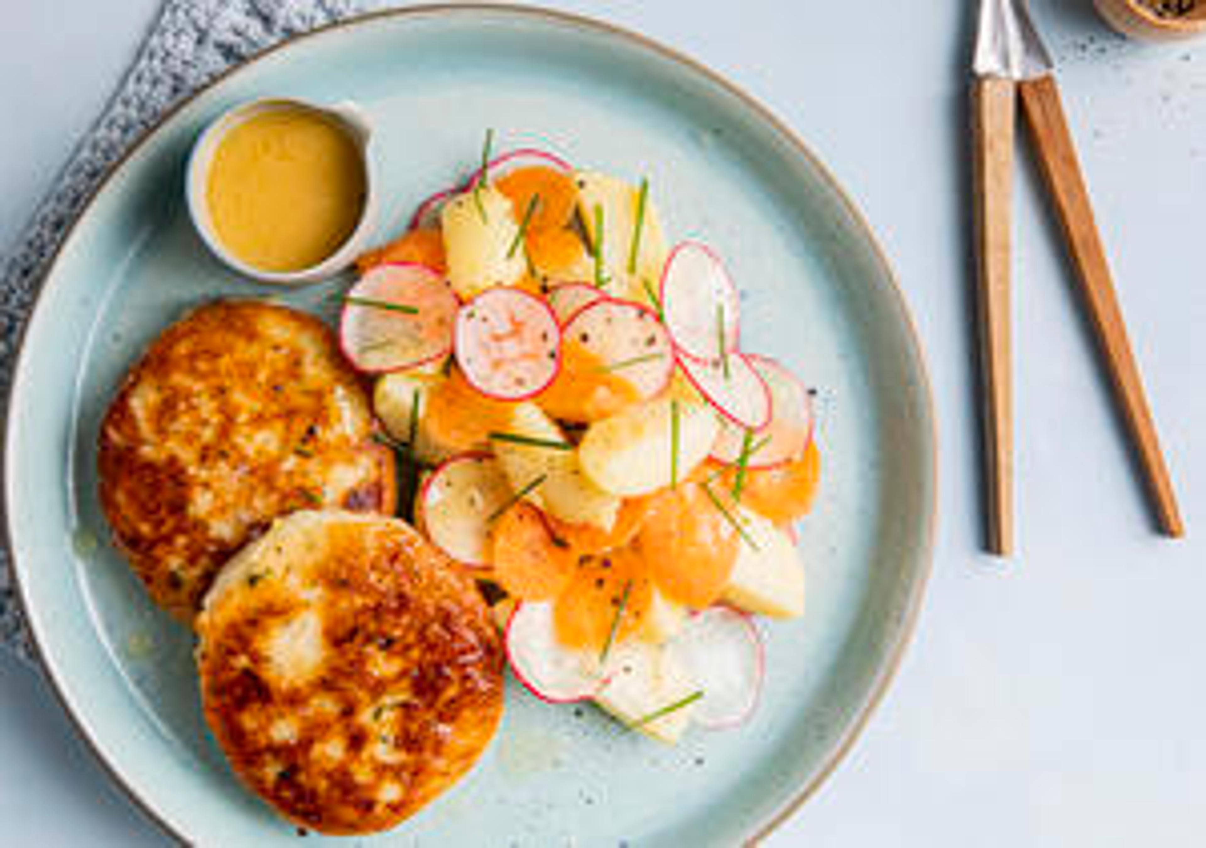 Stekte fiskekaker på et far med potetsalat som inneholder rødbet, gulrot, urter og poteter.