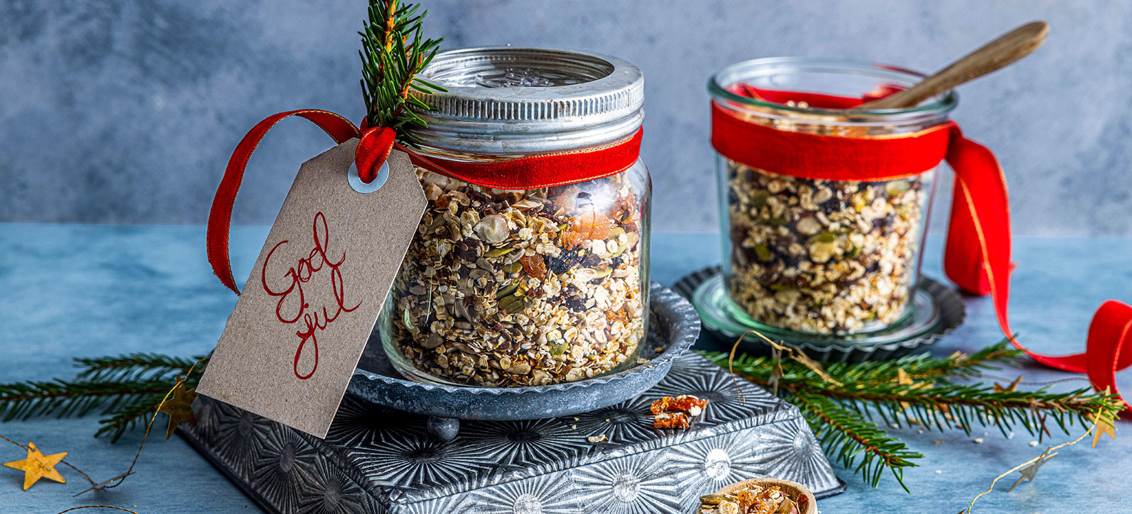 Glasskrukker fylt med müsli, frø og tørket frukt, med treskje og dryss av ingredienser på bordet.