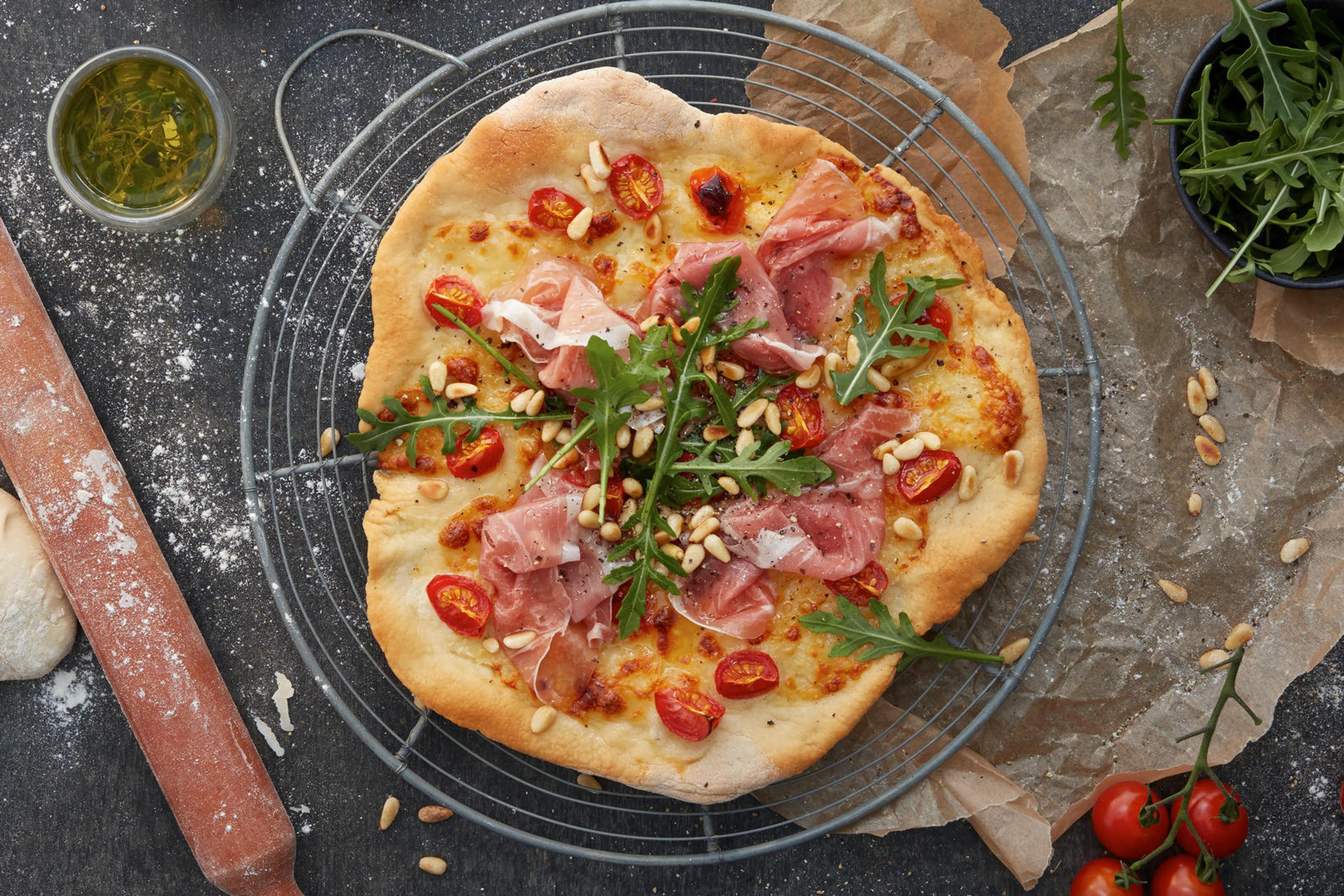 Hjemmelaget pizza, toppet med ost, tomatsaus, pinjekjerner, tynne skiver Prosciutto Crudo (italiensk spekeskinke) og frisk ruccula.