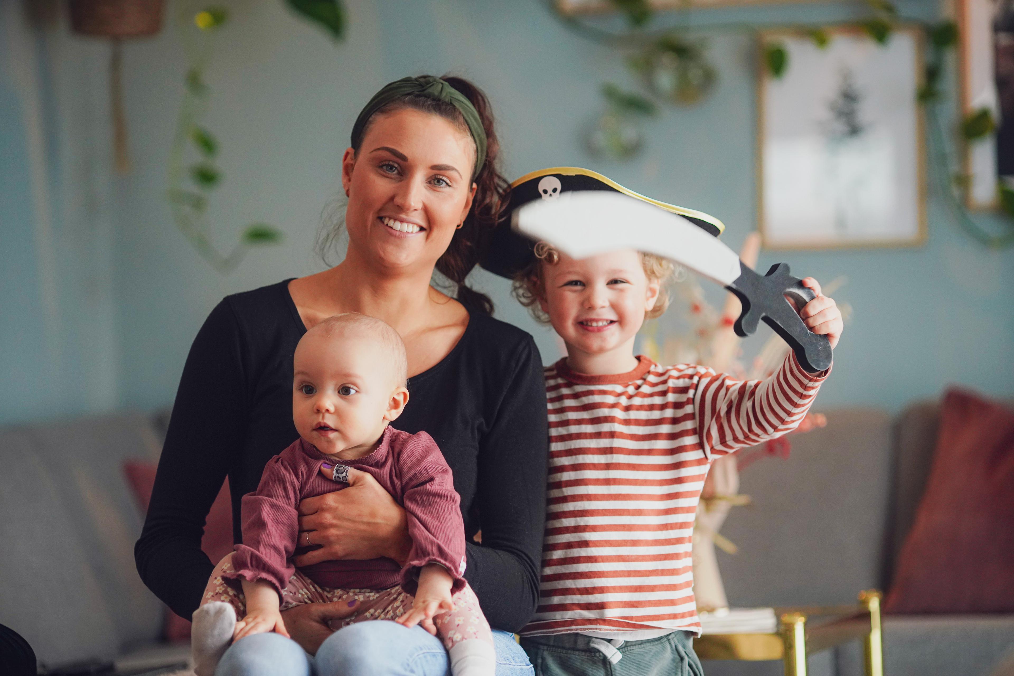 Mamma som smiler, med baby få fanget og liten gutt med sjørøversverd ved siden av