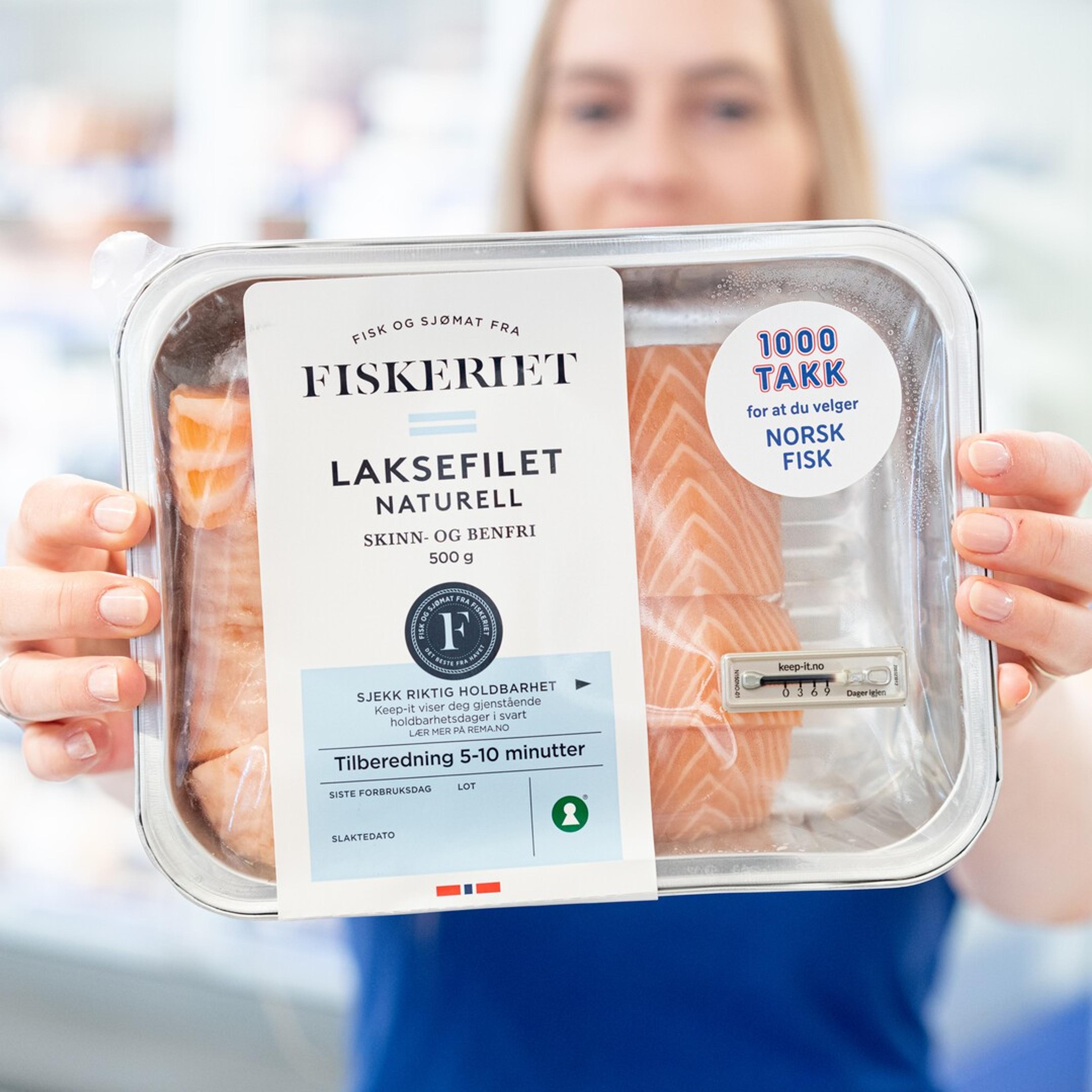 Person holder en pakke med laksefilet fra Fiskeriet foran kamera. Emballasjen inneholder fersk, skinn- og benfri laks og er merket med informasjon om holdbarhet og norsk fisk.