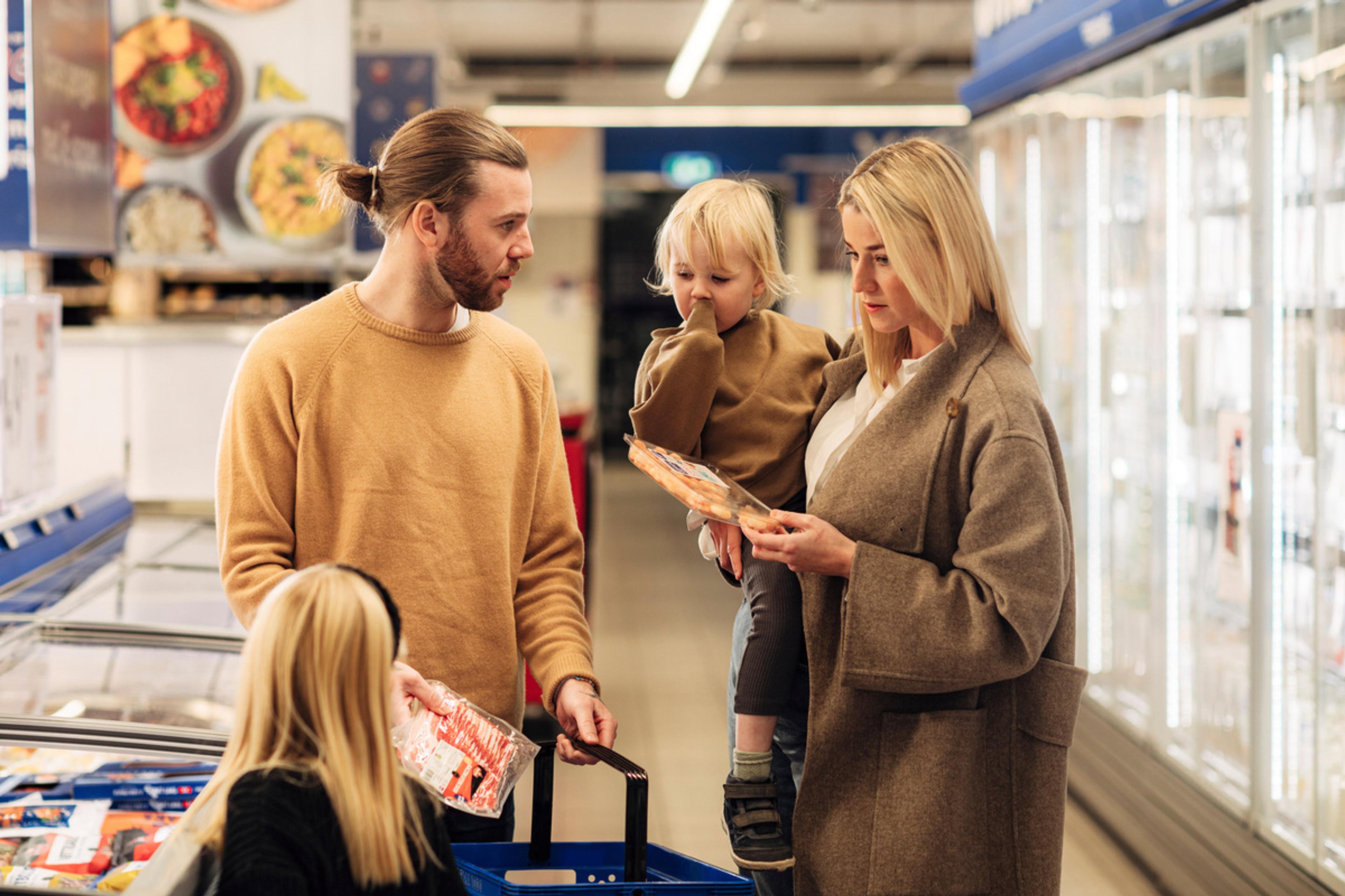 "Familie på fire handler i dagligvarebutikk i fryse- og kjøleavdelingen, mens mor sjekker produktetikett"