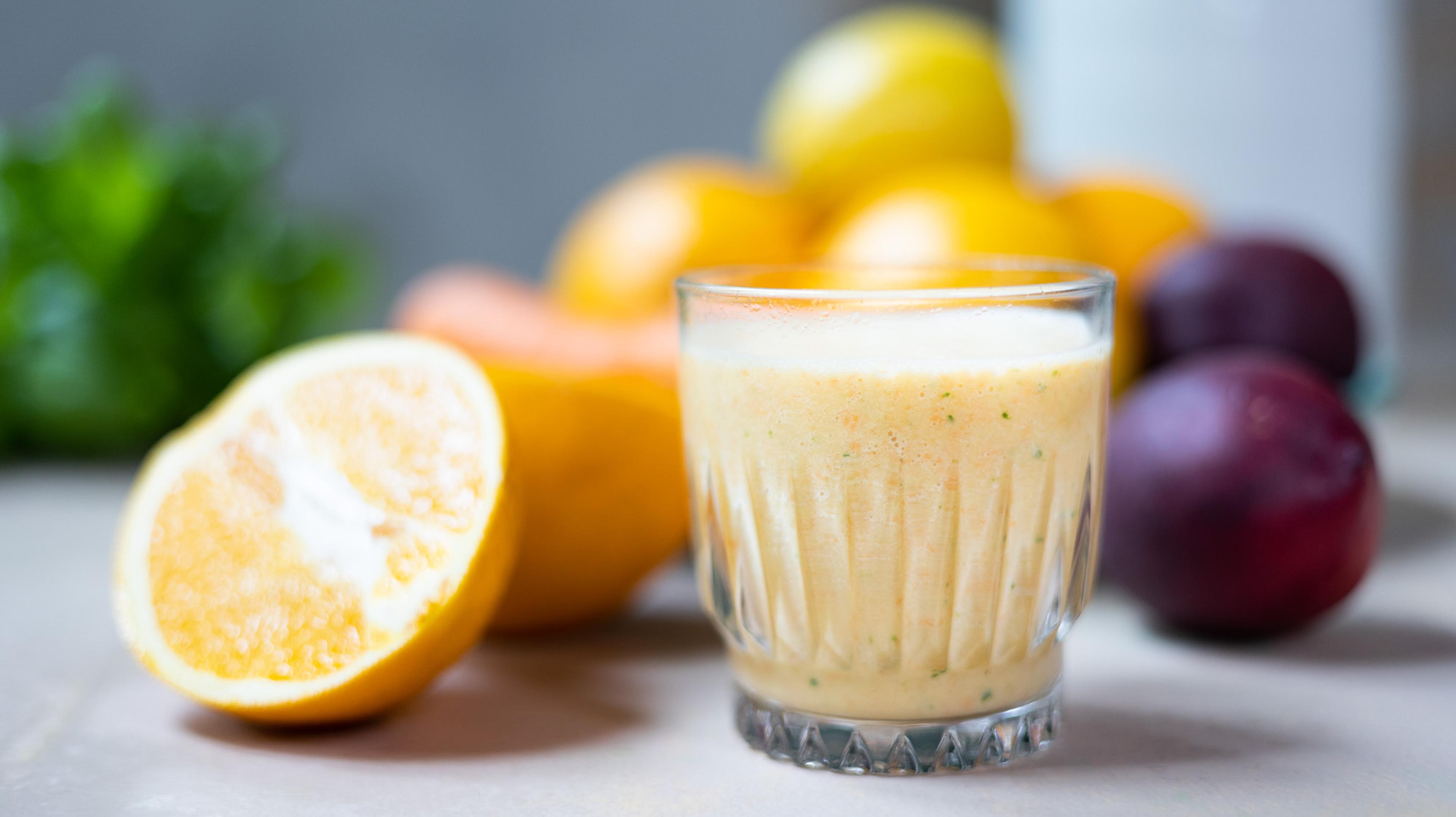 smoothies til trening. appelsinsmoothie i forgrunnen i et glass med frukt og grønt bak