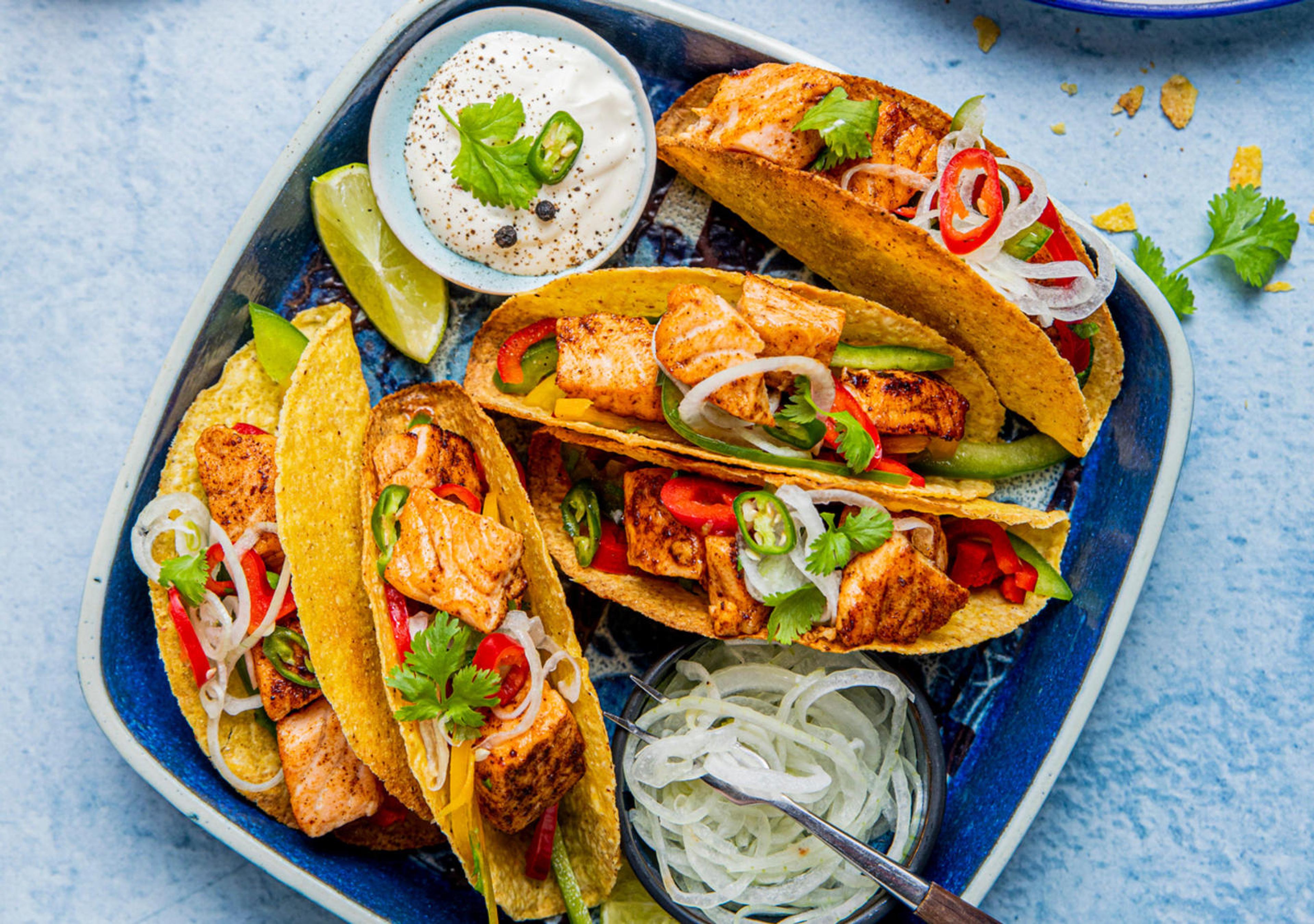 tacoshell fylt med grønnsaker som chili, koriander, vårløk, løk og laks i biter. Serveres med rømme