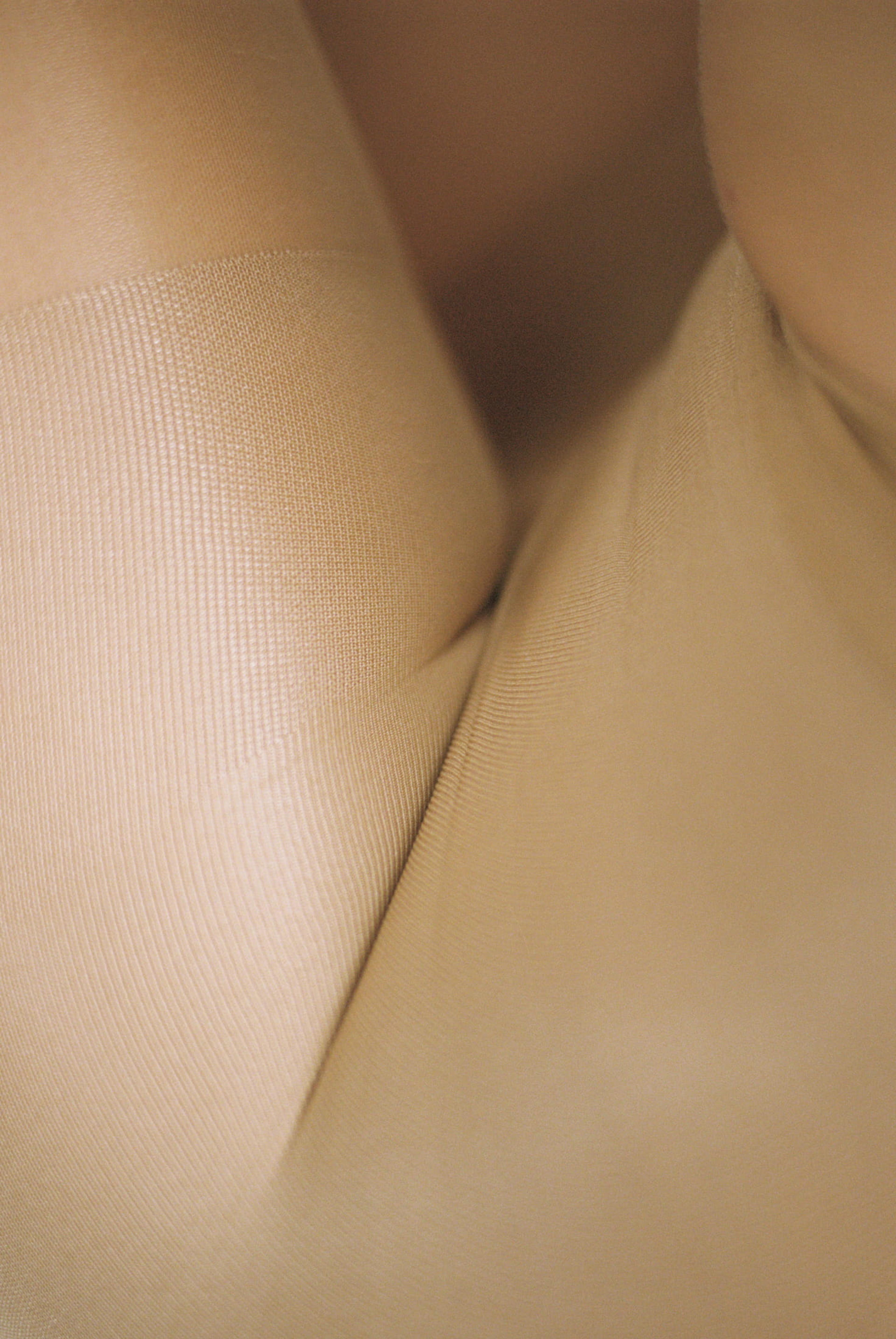 Nærbilde av beige strømpebukse eller tights med finmasket struktur. Bildet fremhever stoffets tekstur, passform og sømløse uttrykk.