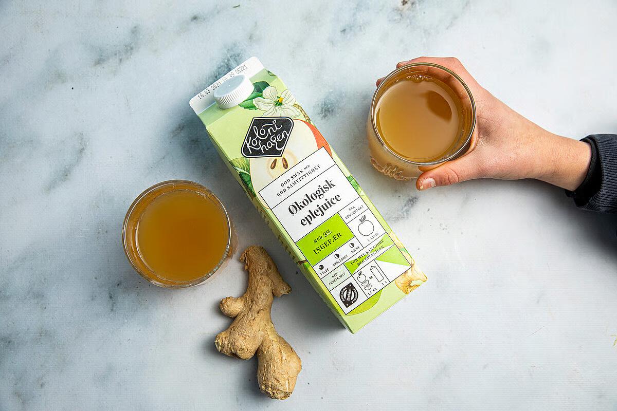 Kartong med Kolonihagens økologiske eplejuice med ingefær, ved siden av ingefærrot og to glass juice.