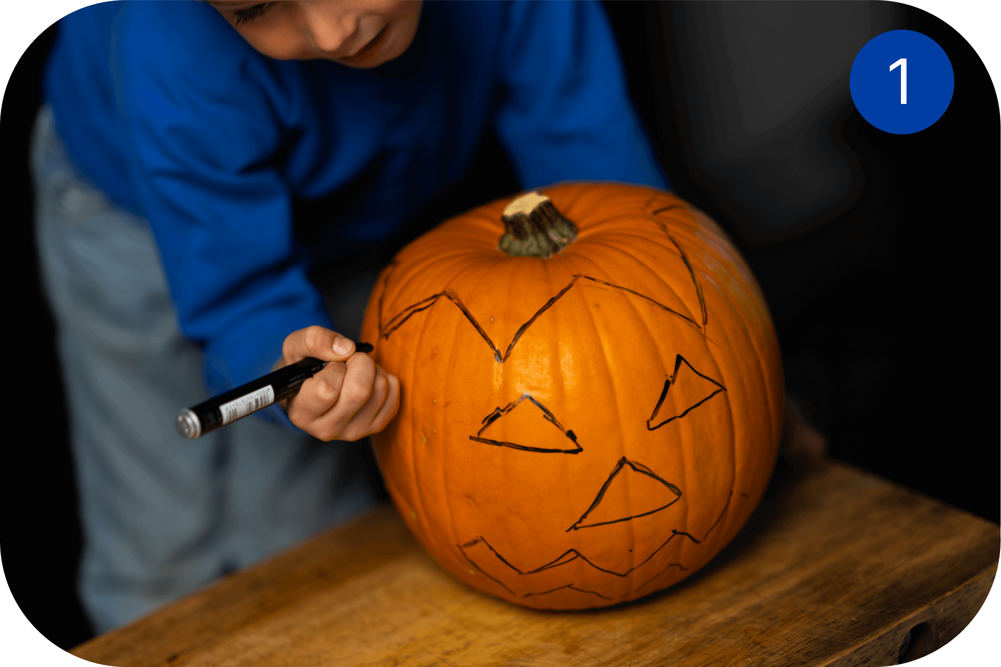 Person tegner ansikt på et gresskar før utskjæring til Halloween.